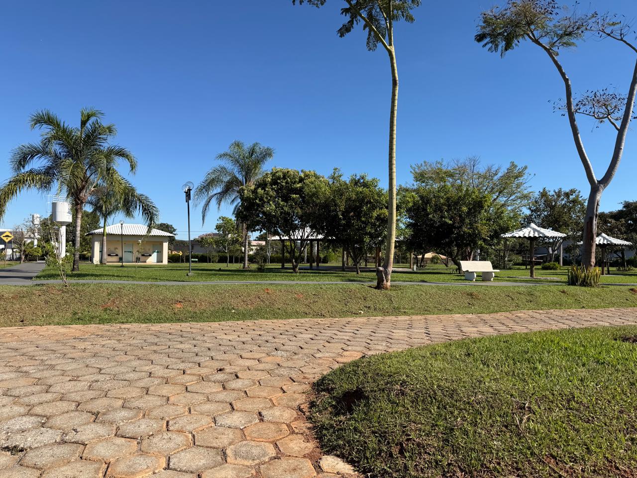 Praça interna com gramado, palmeiras, bancos e quiosques