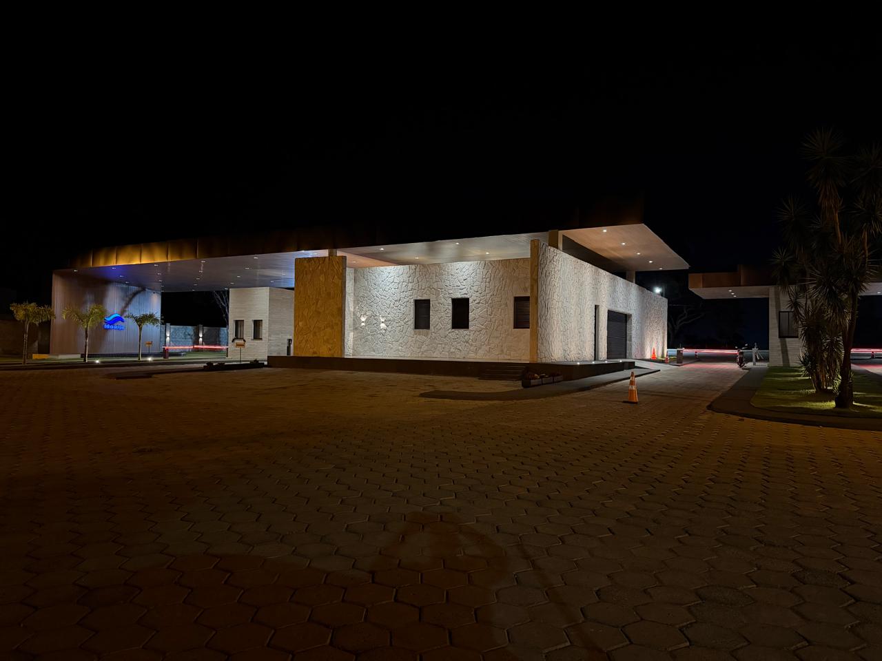 Portaria do condomínio iluminada à noite, com fachada em pedra e madeira